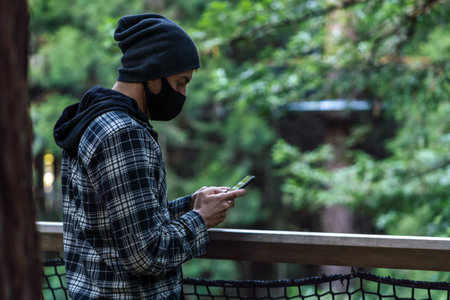 Young man holding mobile phone and wearing face mask on a natural environment.の写真素材