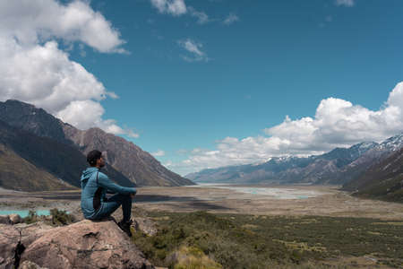 Man sitting on a rock looking at the amazing view of the valley in Mount Cook National park.の写真素材
