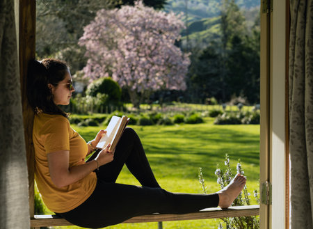 Brunette woman reading a book outside by the window of a cabin on a farm. copy-spaceの写真素材
