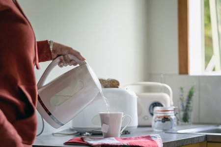 Pouring boiling water on a cup of tea with electric kettle in the morning. Unrecognizable person. close-upの写真素材