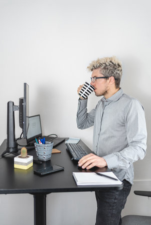Businessman in standing desk working and drinking coffee. Comfort at work concept. portrait photoの写真素材
