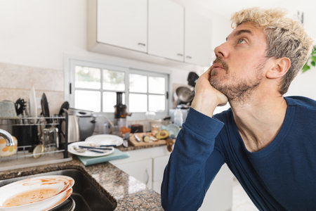 Caucasian man worried about the mess of dirty dished and rubbish in his kitchen in the morning. Close up to his faceの写真素材