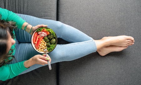 Woman eating vegan food sitting on the couch at home in bare feet. Top view. unrecognizable personの写真素材