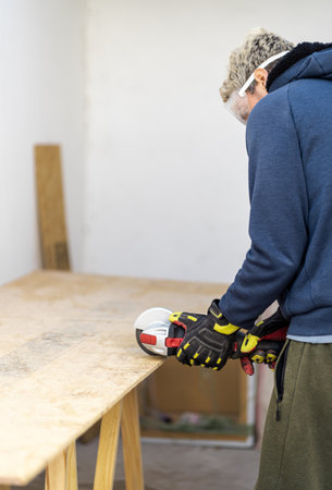 Man cutting wood with electric saw wearing protective gloves and glasses at home. portrait photoの写真素材