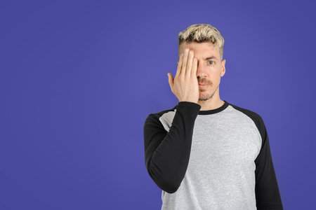 Caucasian man covering half of his face with hand. Portrait-shot. Studio isolated very peri background. Copy space on left sideの写真素材