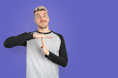 Man standing while asking for time put with his hands on isolated purple background. Isolated purple background studio shotの写真素材