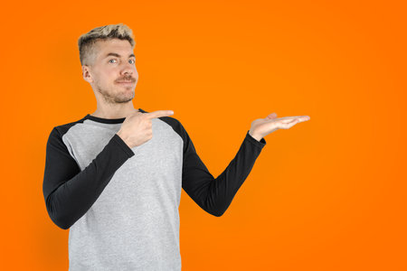 Caucasian young adult man pointing finger at right empty space, showing advertisement on orange isolated backgroundの写真素材