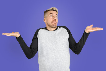 Young adult man rising hands and shrugging shoulders like he doesn't know what to do. Isolated on very peri color backgroundの写真素材