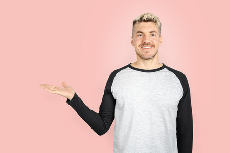 Portrait of adult young man smiling and showing something on his palm for copy space advertising product. pink background studio shotの写真素材