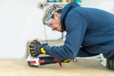 Caucasian cutting wood with electric circular saw and wearing protective gloves and glasses. Carpentry at home conceptの写真素材