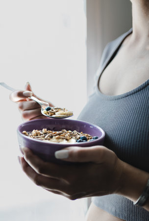 close up of woman hands holding muesli bowl while standing next to the window in the morning. Healthy eating concept. Unrecognizable person. portrait photographyの写真素材