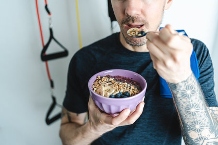 Young adult man eating nutritious granola bowl after workout at home. Close up caption. unrecognizable personの写真素材