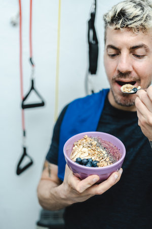 Caucasian man eating granola and smoothie bowl after training and workout at home. Fitness and healthy lifestyle concept. portrait photographyの写真素材