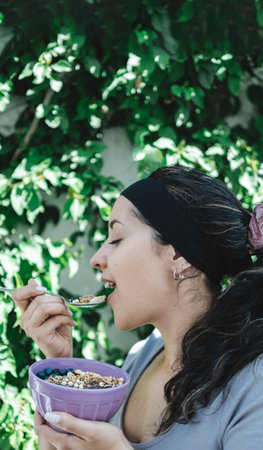 Latina woman in profile standing outdoors while eating granola bowl. Portrait photography. copy-spaceの写真素材