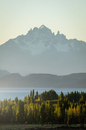 Mountain with snowy peak on a sunny summer day surrounded by a lake and pine trees. Portrait photography. The Ancients, Patagonia, Argentinaの写真素材