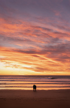 Couple silhouette embracing each other looking at dramatic sunrise at the beach. Copyspace. portrait photographyの写真素材