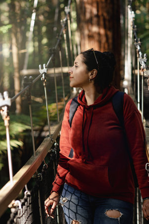 Young latin maerican woman walking through suspension bridge among redwood tree. portrait photographyの写真素材