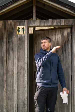 Caucasian man going out rustic outdoors toilet with toilet paper in his hand and smelling bad. portrait photographyの写真素材