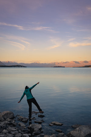 Woman balancing on the shore of lake at sunset. Mountainside landscape. Lake Tekapo, New Zealandの写真素材