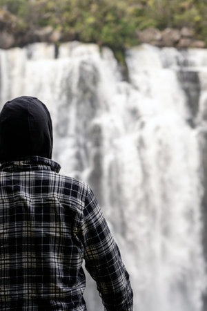 Young man with hoodie admiring huge waterfall in the middle of forest. inspirational conceptの写真素材
