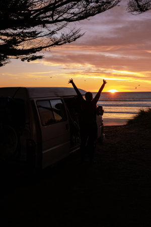 Man stretching arms next to his camper van at sunrise at the beach. portrait photographyの写真素材