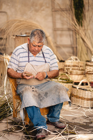 Mature craftsman sitting on his char while working on her wicker baskets at workshop. Latin American culture and arts concept. portrait photographyの写真素材