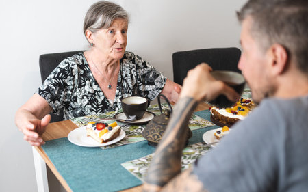 Caucasian senior woman having a chat with her son during tea time. Select focus. Supporting and volunteering senior citizensの写真素材