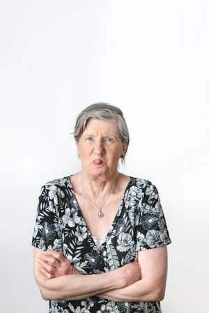 Old senior grey-haired woman doing mocking gesture while sticking out tongue. Portrait vertical photography on white backgroundの写真素材