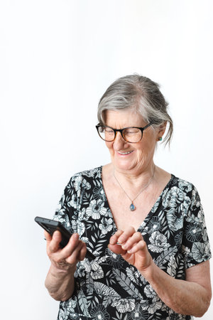 Senior lady in her 70's using smart phone and smiling over isolated white background. portrait photographyの写真素材