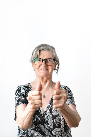 Happy old gray hair woman doing thumbs up while smiling at camera. Vertical photography over white backgroundの写真素材