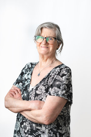 Smiling senior woman posing and looking at camera with arms crossed over isolated white background. Vertical photography studio shotの写真素材