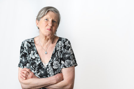 Senior woman sticks out her tongue on a mocking face while looking at camera. Isolated white background studio shot. Copy Space on right sideの写真素材