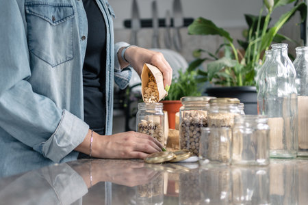 Close up of woman hand filling recycled glass jars in the kitchen. Plastic free and sustainability at home concept. Copy space for text belowの写真素材