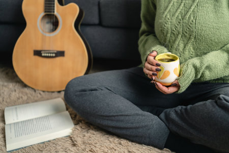 Woman sitting on the floor of living room while drinking hot coffee and reading a book during winter time. Call for winter concept. unrecognizable personの写真素材