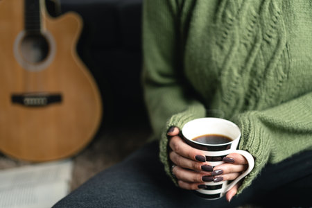 Close up of woman hand wearing winter sweater holding coffee cup while enjoying a moment of solitude at home. Leisure time and holidays in winterの写真素材