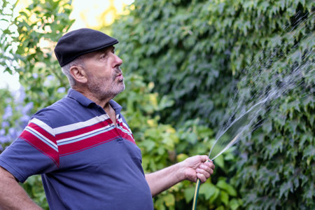 Mature retired man whistles while watering his green garden at home. Copy Space on right for advertisementの写真素材