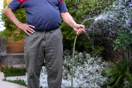 Senior man watering plants in his garden. Close up shot with unrecognizable person. Copy space on the rightの写真素材