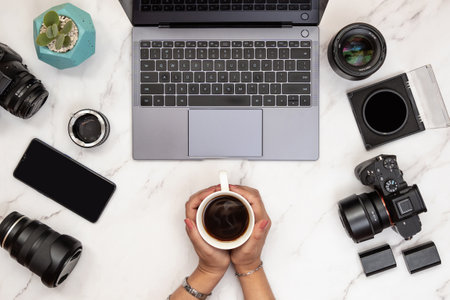 White marble layout of photographer workspace with woman hands holding hot coffee on a mug. Photographers freelance concept top viewの写真素材