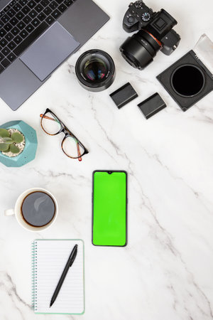 Modern white marble photographer workspace with laptop, camera, notepad, hot cup of coffee and mobile with green screen for chroma key. Vertical top view. Photography and freelance work conceptの写真素材