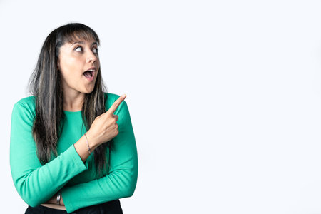 Hispanic brown haired woman with surprised gesture pointing to the side on a white background for placing advertisement. Copy space on right sideの写真素材