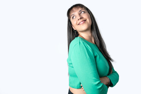 Pretty Latin woman with her arms crossed and looking up in lateral position on white background. Copy space on left sideの写真素材
