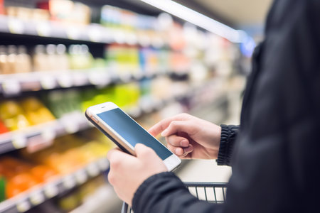 Close up shot of unrecognizable person using smart phone in supermarket. Generative AIの素材