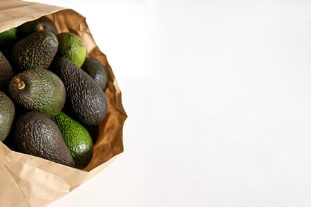 A paper bag full of avocados top view over white layout with copy spaceの素材