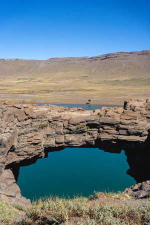 Stone bridge arches over a pool of turquoise water, with a vast, arid landscape. Caviahue, Neuquen, Argentinaの写真素材