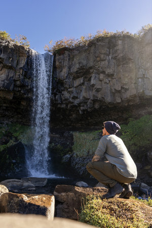 Tourist man in a beanie admiring Cascada de la Usina waterfall over rocky cliffs. Caviahue, Neuquen, Argentinaの写真素材