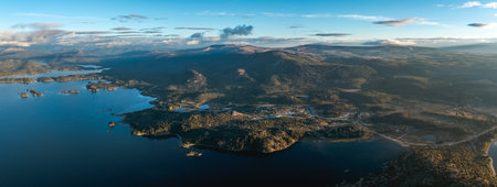 Aerial panoramic reveals Lake Alumine with several islands, surrounded by forested hills and mountains under a partly cloud sky. Villa Pehuenia, Neuquen, Argentinaの写真素材