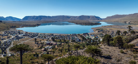 Panoramic view of Caviahue village by the lake surrounded by Araucaria trees, with mountains in the background under clear sky. Neuquen, Argentinaの写真素材