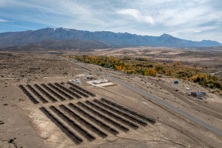 Aerial view of solar power plant in an arid landscape with mountains and autumn colored trees in the background under cloudy sky. El Alamito, Neuquen, Argentinaの写真素材