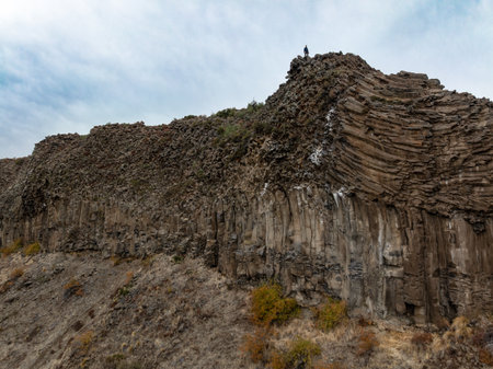 Distant figure atop dramatic basalt rock formations under an overcast sky. Alumine, Neuquen,...