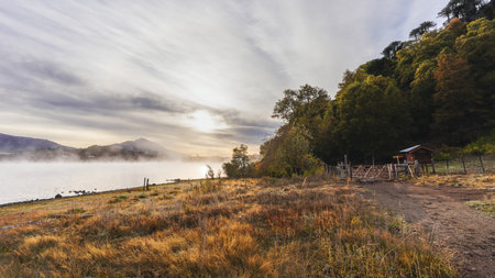 Morning golden mist over a lake surrounded by autumn foliage and mountains. Patagonian landscapeの写真素材